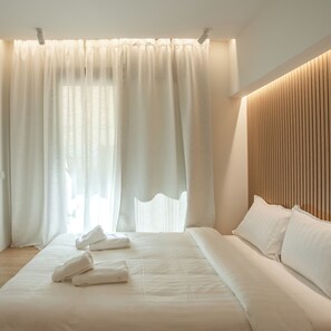 A modern hotel room with a large bed, white linens, and a wooden headboard. - Mini Suites Trikala (Trikala)