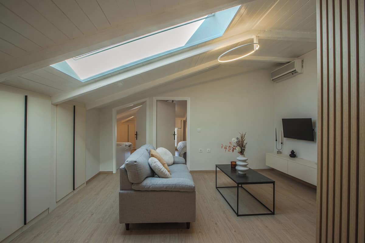 A modern living room with a skylight, a sofa, a coffee table, and a TV on the wall.