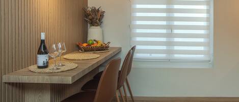 Un comedor con una mesa de madera, sillas, una botella de vino y una cesta de frutas.