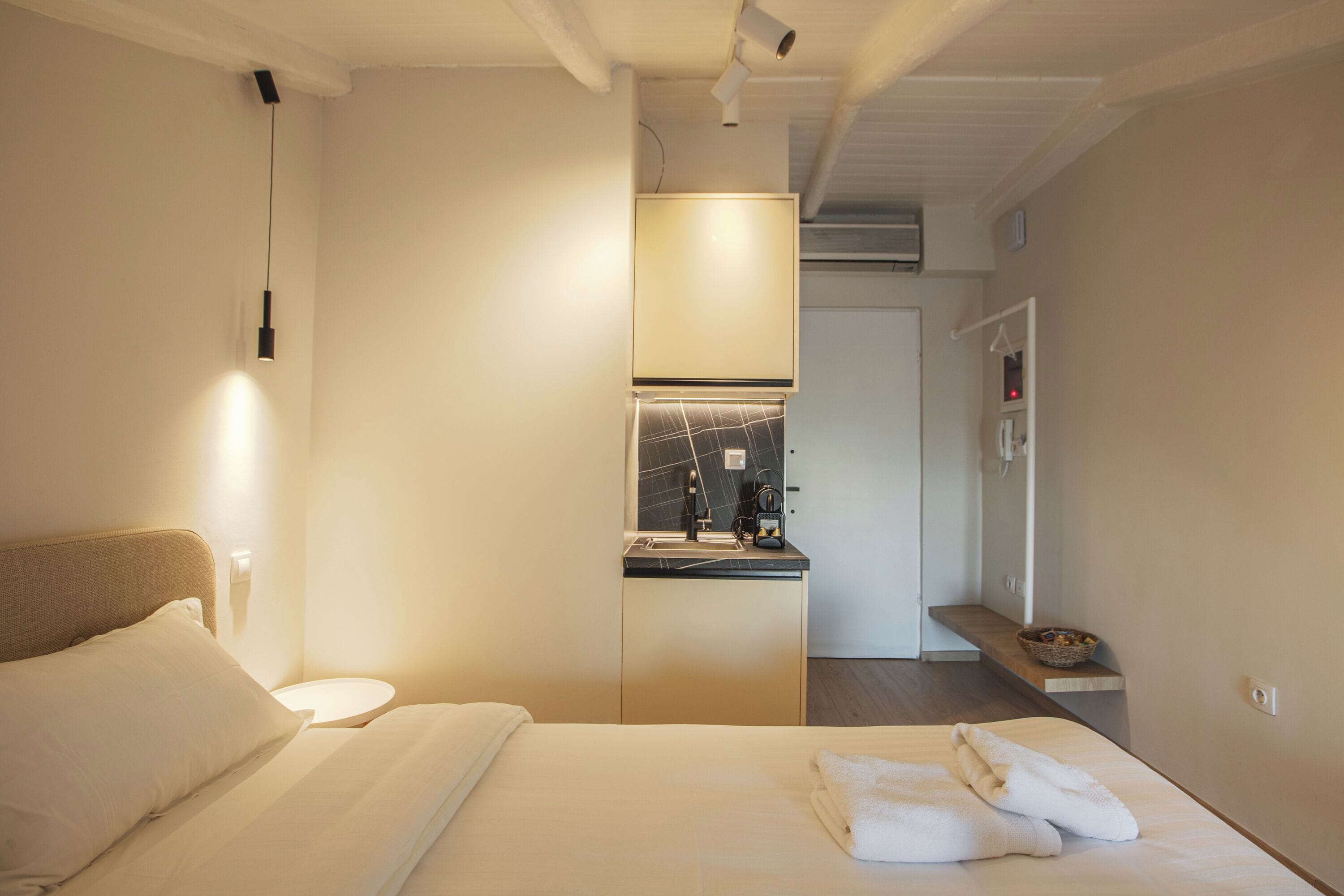 Ein Hotelzimmer mit Bett, Nachttisch, einer kleinen Küchenzeile und einem im Hintergrund sichtbaren Badezimmer.