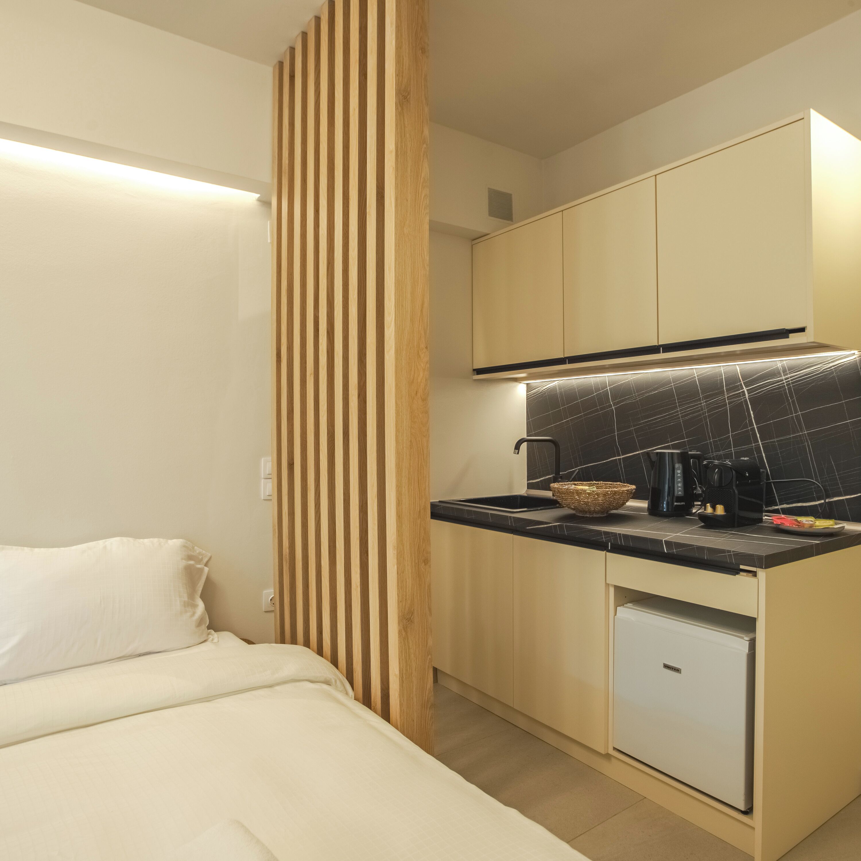 Una cocina compacta con encimera negra, un refrigerador pequeño y una separador de madera.