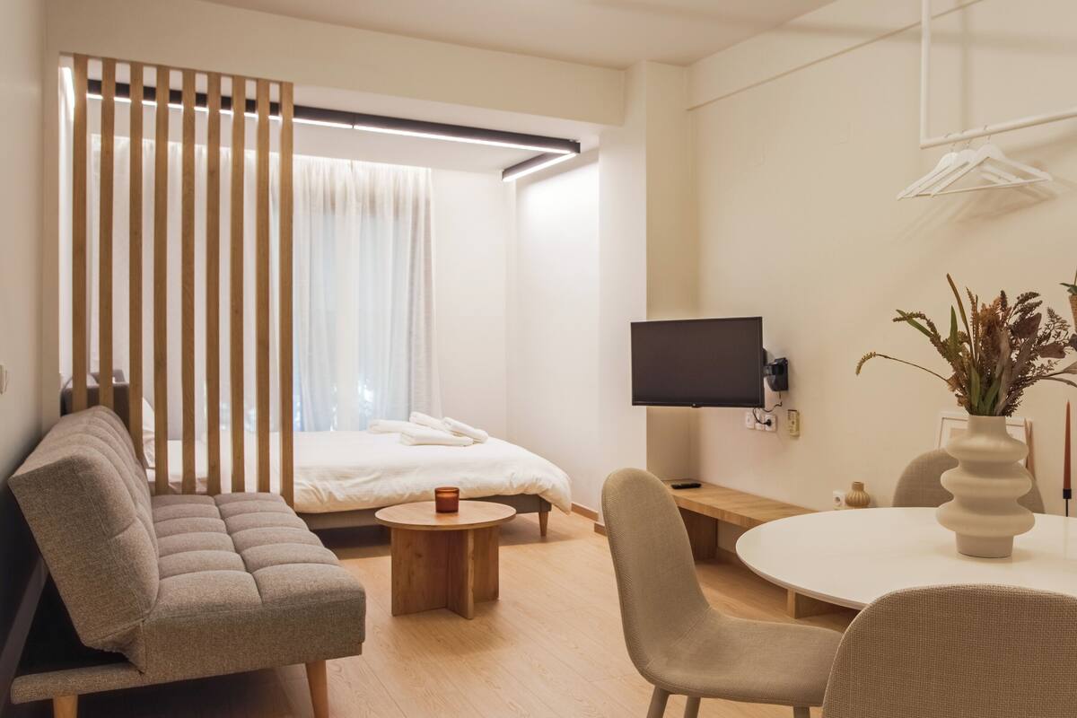 A modern hotel room with a bed, a sofa, a TV, a desk, and a dining table.