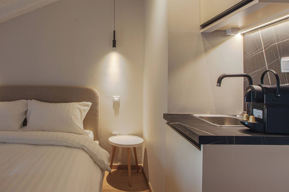 A compact hotel room with a bed, a small round table, a sink, and a kitchenette.