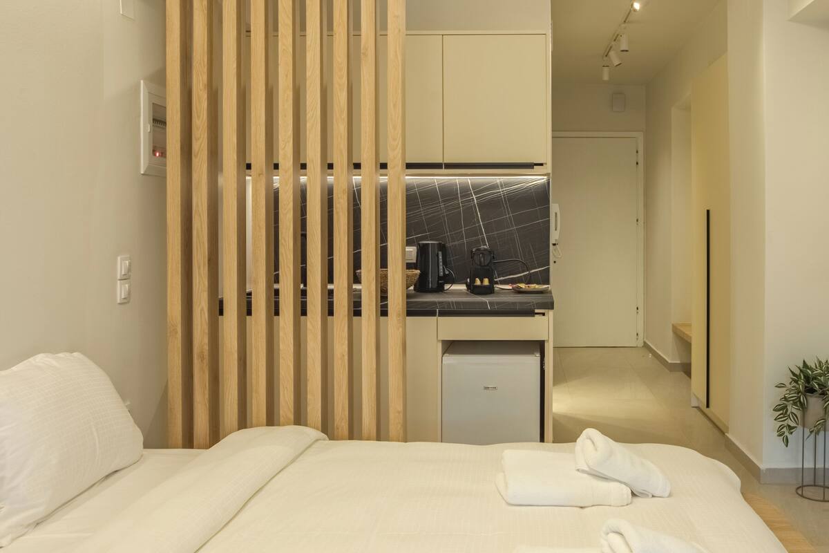 A modern hotel room with a bed, a small kitchenette, and a sliding wooden partition.