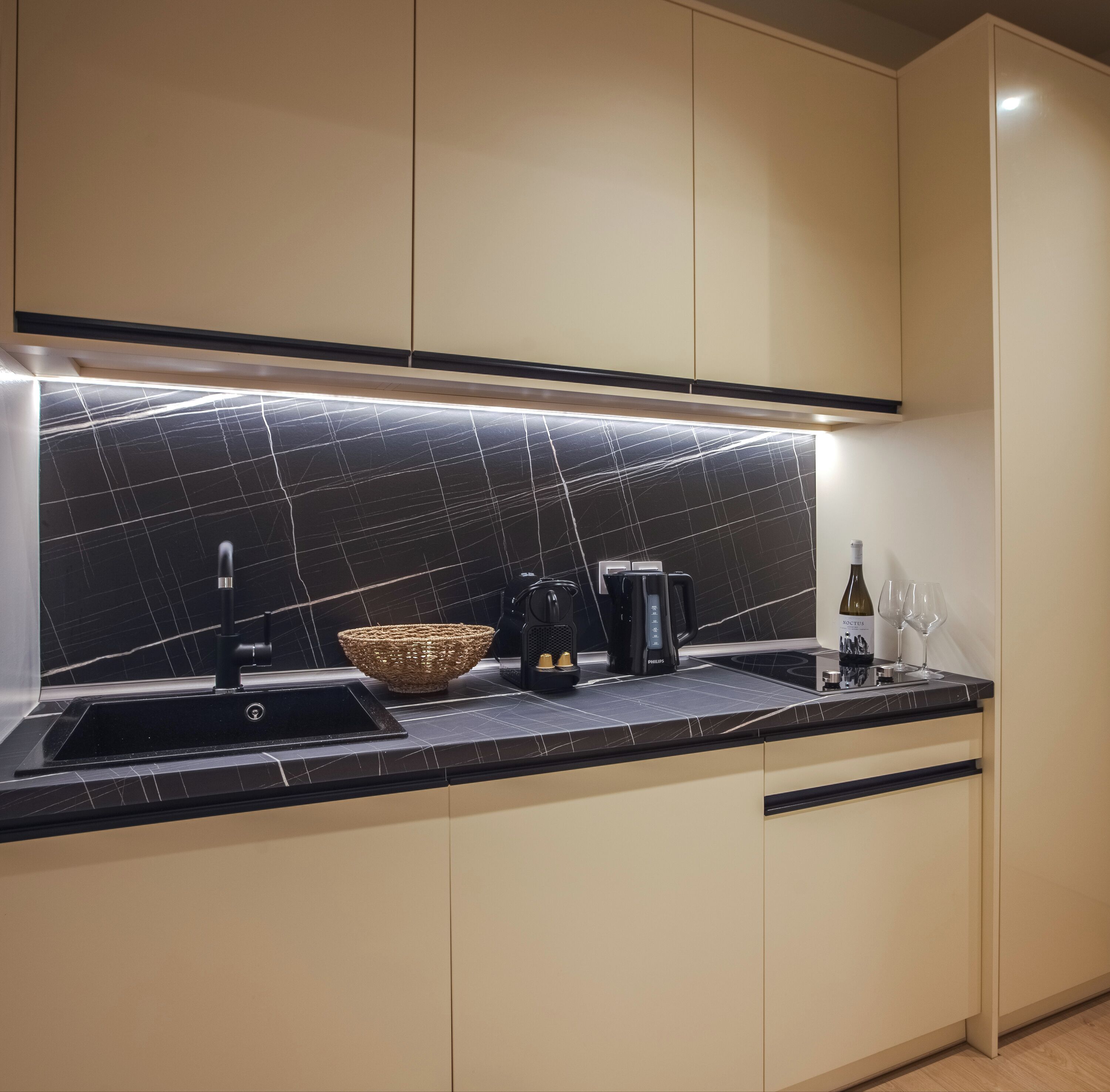 A modern kitchen with a black marble backsplash, a black countertop, and beige cabinets.