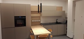 A compact kitchen with a built-in oven, a countertop sink, and a dining area with chairs. - Apartment in Villafranca - Politeama, Palermo (Palermo)