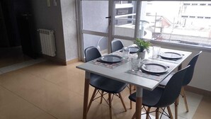 A dining area with a table set for four, chairs, a radiator, and a window with a view of buildings. - Mirando el cerro (Salta)