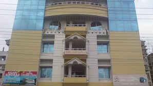A multi-story building with a yellow facade, several balconies, and various commercial signs including a cruise ship advertisement. - Urmee Guest House Coxs Bazar (Cox's Bazar)