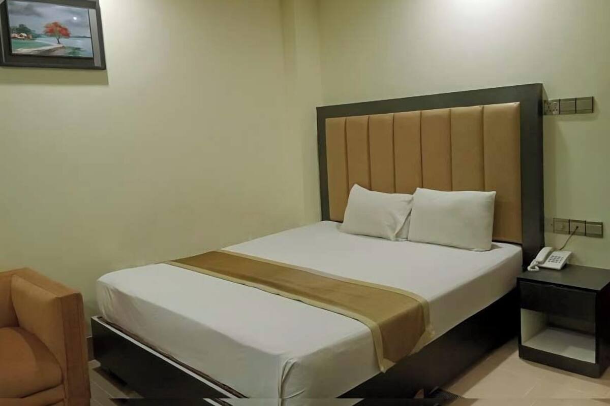 A neatly made bed with a headboard, a bedside table with a phone, and a chair.
