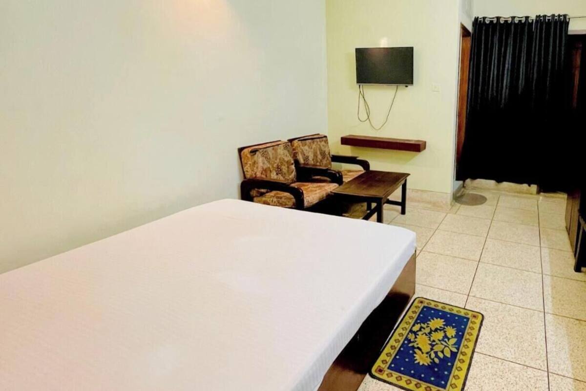 A room with a bed, a sofa, a TV mounted on the wall, and a ceiling fan.