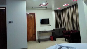 A modern hotel room with a bed, a desk, a TV, and a curtain. - Urmee Guest House Coxs Bazar (Cox's Bazar)