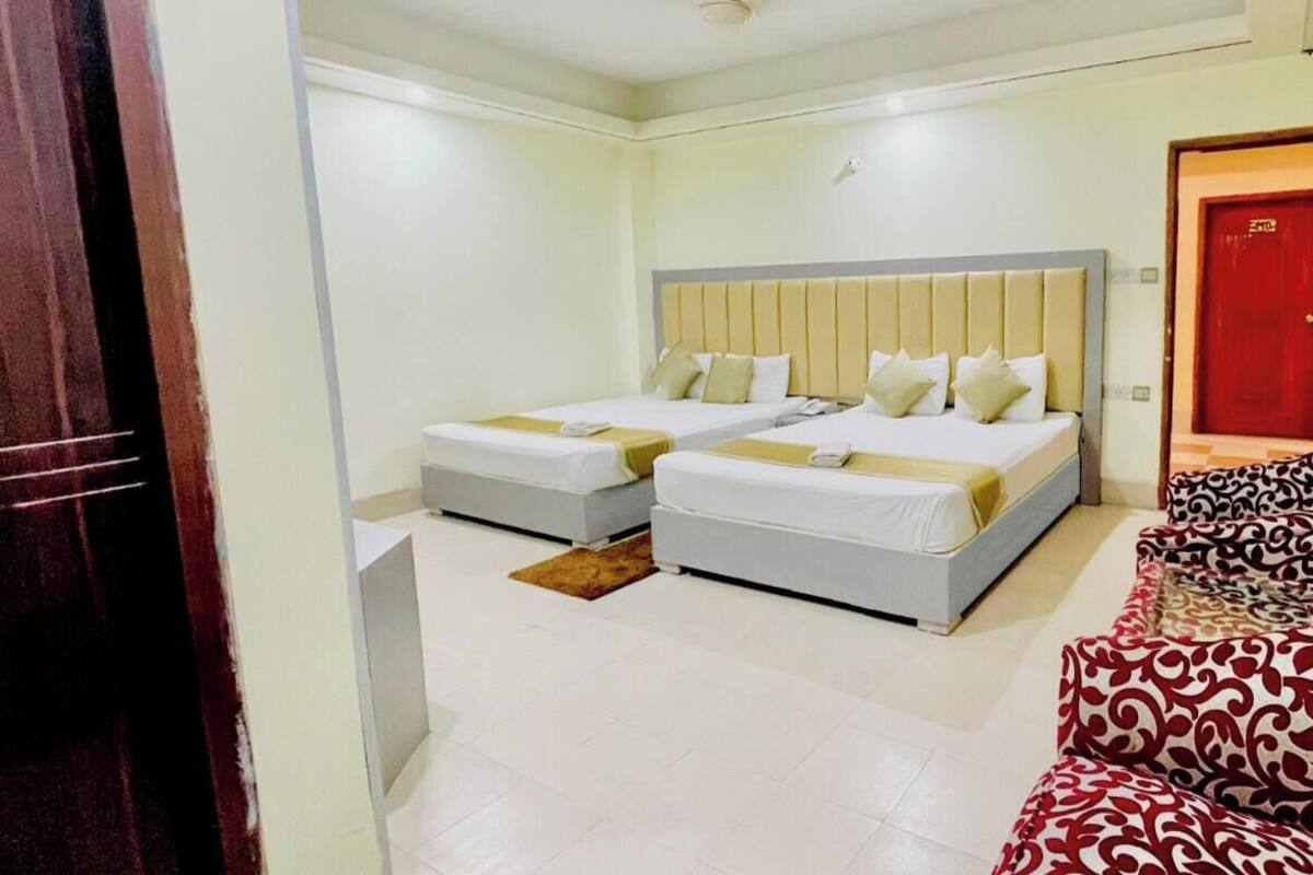 A hotel room with two beds, a red door, and a patterned sofa.