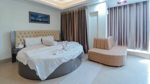 A modern hotel room with a large bed, a curved sofa, a nightstand, and a painting on the wall. - Urmee Guest House Coxs Bazar (Cox's Bazar)