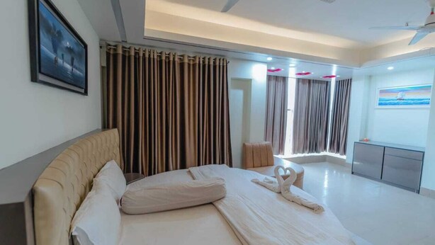 A modern hotel room with a large bed, curtains, a ceiling fan, and a painting on the wall. - Urmee Guest House Coxs Bazar (Cox's Bazar)