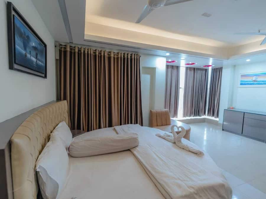 A modern hotel room with a large bed, curtains, a ceiling fan, and a painting on the wall.