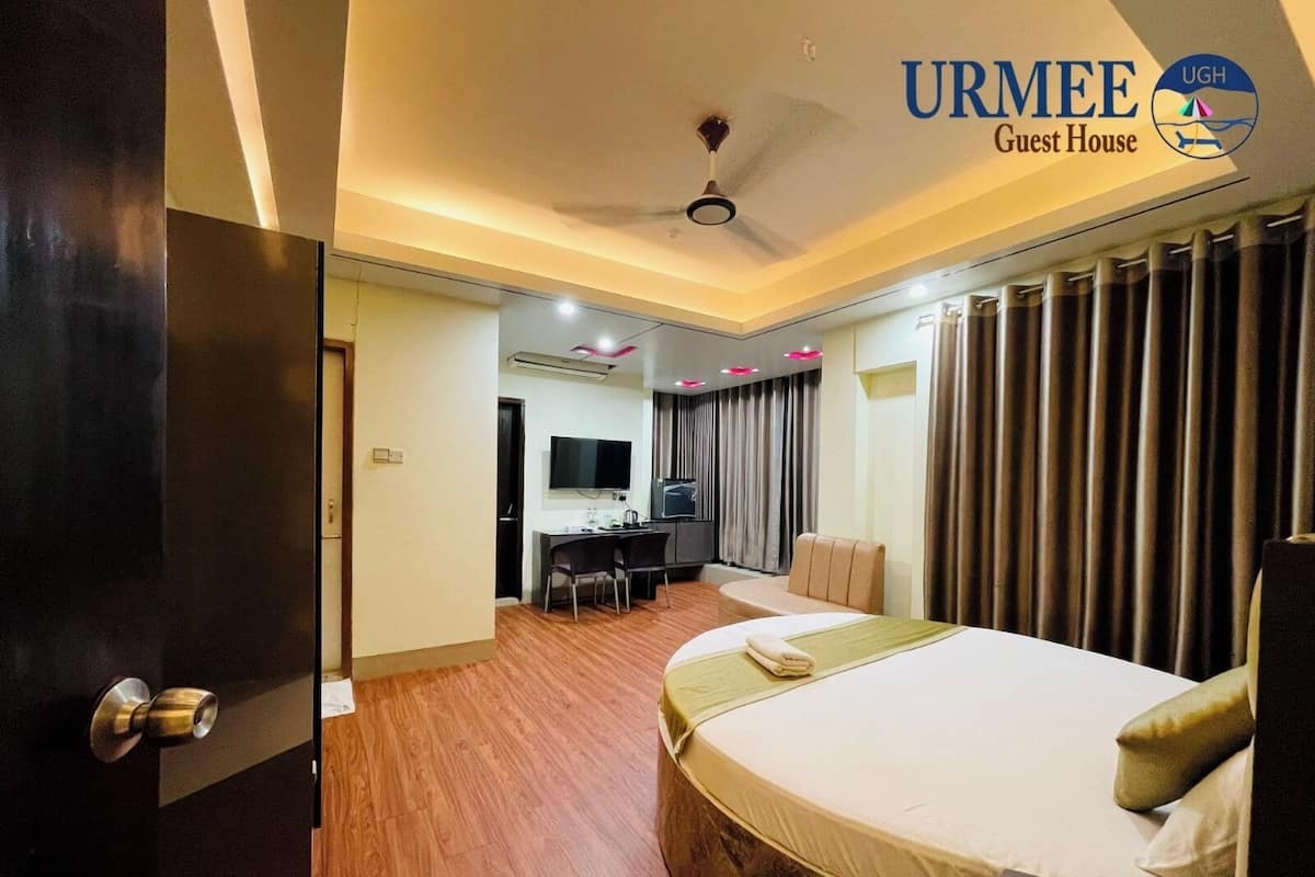 A hotel room with a bed, a desk with a chair, a television, and a ceiling fan.