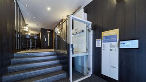 A modern hotel lobby with a glass elevator, a check-in kiosk, and a staircase leading to another floor. -  B48 Oviedo Ópera (Oviedo)