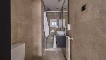 Un baño moderno con cabina de ducha de vidrio, inodoro blanco y lavabo con espejo arriba.