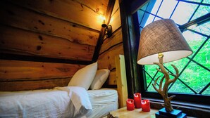 Una habitación de cabaña de madera con una cama, una mesa con velas y una lámpara con base en forma de árbol.