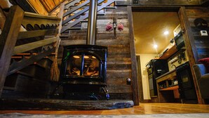 Una escalera de madera que conduce a una habitación con estufa de leña, un revestimiento de madera y un estante con objetos.