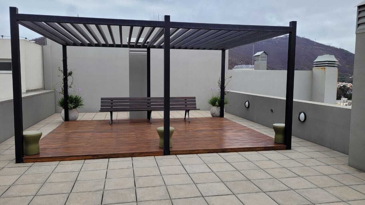 A covered outdoor seating area with a wooden bench and two potted plants.