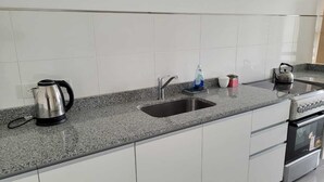 Egy konyha gránit munkalappal, rozsdamentes acél mosogatóval, vízforralóval és beépített sütővel.