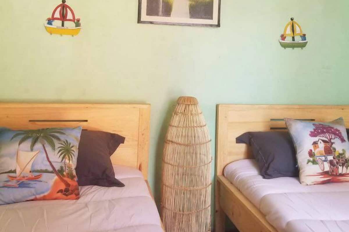 A room with two beds, each with a different pillow design, a woven basket, and a framed picture on the wall.