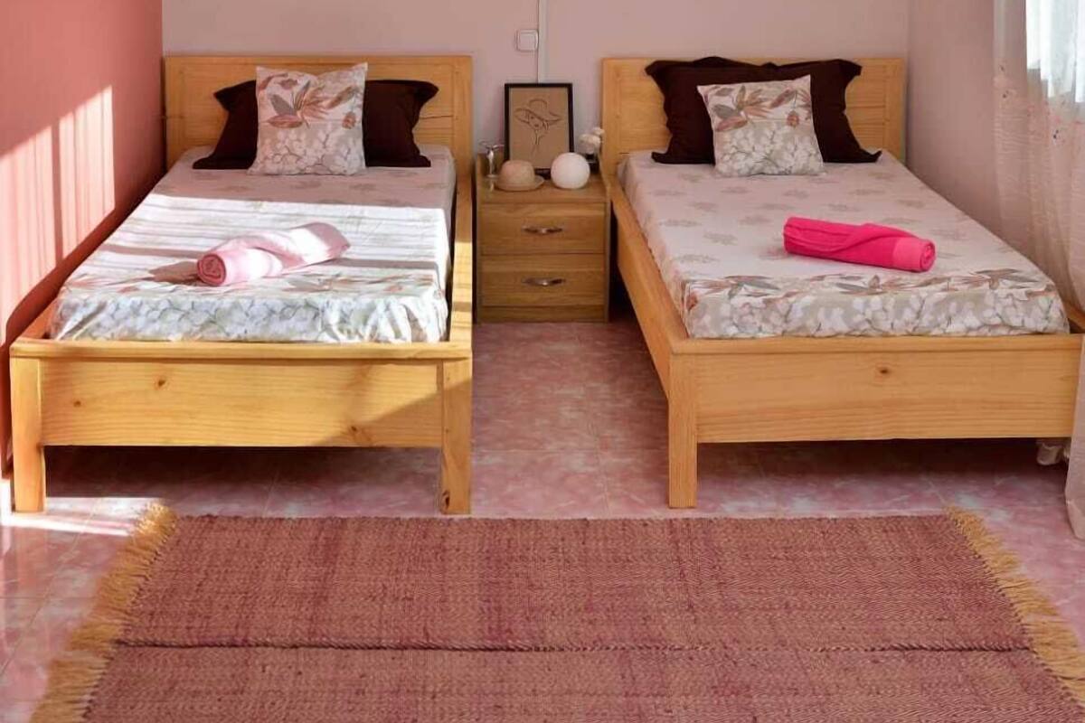 A bedroom with two wooden beds, a hanging light fixture, a nightstand, and a window with curtains.