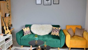A living room with a green sofa, a yellow armchair, and a white furry throw. There are framed pictures on the wall and a guitar leaning against the wall. - Auberge Iorenantsoa (Talata Volonondry)
