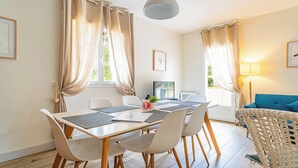 A modern living room with a dining area, featuring a sofa, a table with chairs, and a lamp. - DOMAINE DU FLAMAND - Gîte JEAN-PETIT (Naujac-sur-Mer)