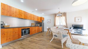 A modern kitchen with wooden cabinets, a dining area with wicker chairs, and a TV in a living space. - DOMAINE DU FLAMAND - Gîte JEAN-PETIT (Naujac-sur-Mer)