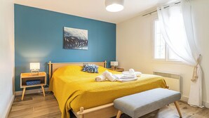 A bedroom with a bed, bedside tables, a bench, a painting, and a window with curtains. - DOMAINE DU FLAMAND - Gîte JEAN-PETIT (Naujac-sur-Mer)