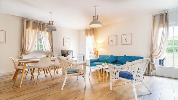 A modern living room with a blue sofa, wicker chairs, a dining table with chairs, and a large window with curtains. - DOMAINE DU FLAMAND - Gîte JEAN-PETIT (Naujac-sur-Mer)