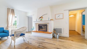 A living room with a fireplace, a blue sofa, a wicker chair, and a wooden floor. - DOMAINE DU FLAMAND - Gîte JEAN-PETIT (Naujac-sur-Mer)