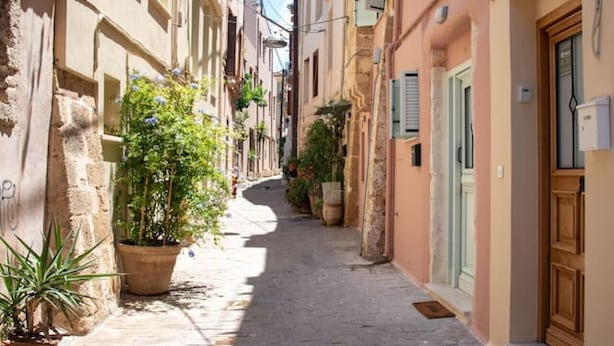 A narrow cobblestone street lined with traditional buildings, some with shutters and potted plants.