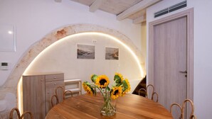 A dining area with a wooden table, wicker chairs, and a vase with sunflowers. There is a wooden cabinet and a door in the background.