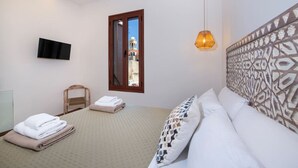 A bedroom with a bed, a TV mounted on the wall, a window with a view of a building, and a patterned headboard.
