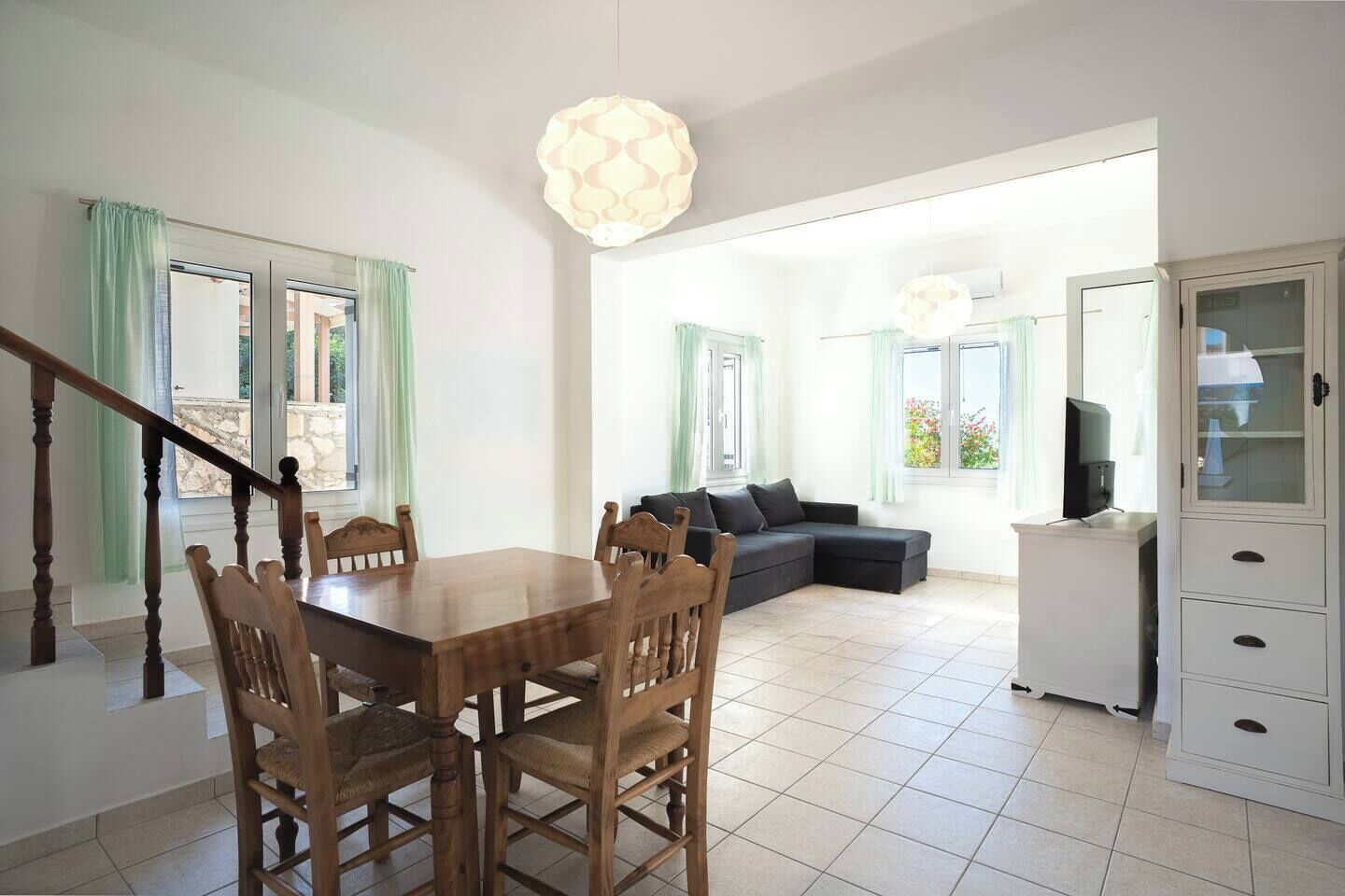 A spacious living area with a dining table, wooden chairs, a sofa, and a TV on a cabinet.