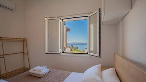 Une chambre d’hôtel avec un lit, une fenêtre donnant sur la mer et un étendoir en bois.