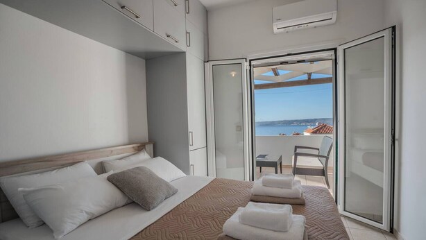 Une chambre d’hôtel moderne, dotée d’un lit, d’un balcon avec vue sur la mer et d’une porte-fenêtre coulissante.