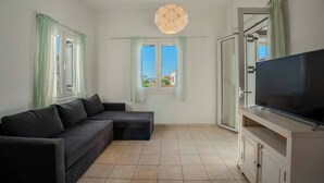 Un salon moderne avec un canapé d’angle, un téléviseur à écran plat et une grande fenêtre donnant sur des immeubles.