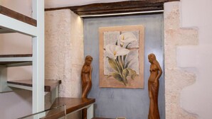 Een trap met houten treden en glazen leuningen, gesierd door twee houten sculpturen en een ingelijste botanische illustratie aan de muur.