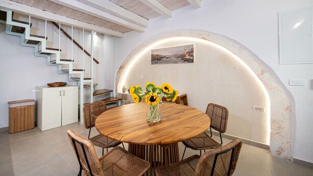 Een eetruimte met een ronde houten tafel, rieten stoelen en een vaas met zonnebloemen.