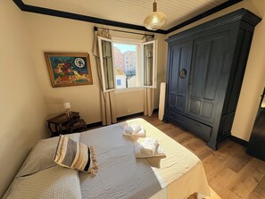 A bedroom with a bed, a wardrobe, a window, and a painting on the wall.