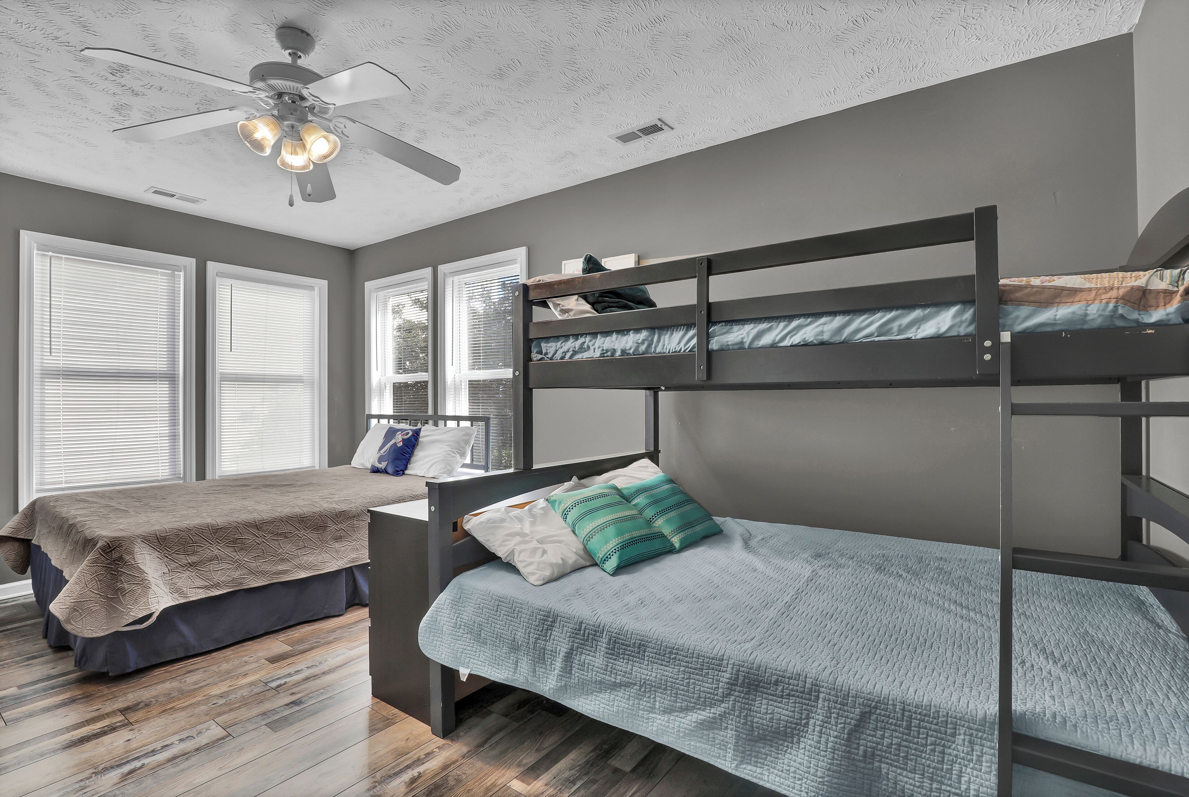 A bedroom with two bunk beds, a ceiling fan, and large windows.