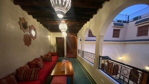 A corridor with a red sofa, a wooden table, and a patterned floor. - Riad Prada (Marrakech)
