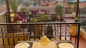 A rooftop terrace with a table set for two, overlooking a cityscape during sunset. - Riad Prada (Marrakech)