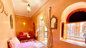 A bedroom with a bed, a window with decorative iron bars, a wall-mounted mirror, and a chandelier. - Riad Prada (Marrakech)