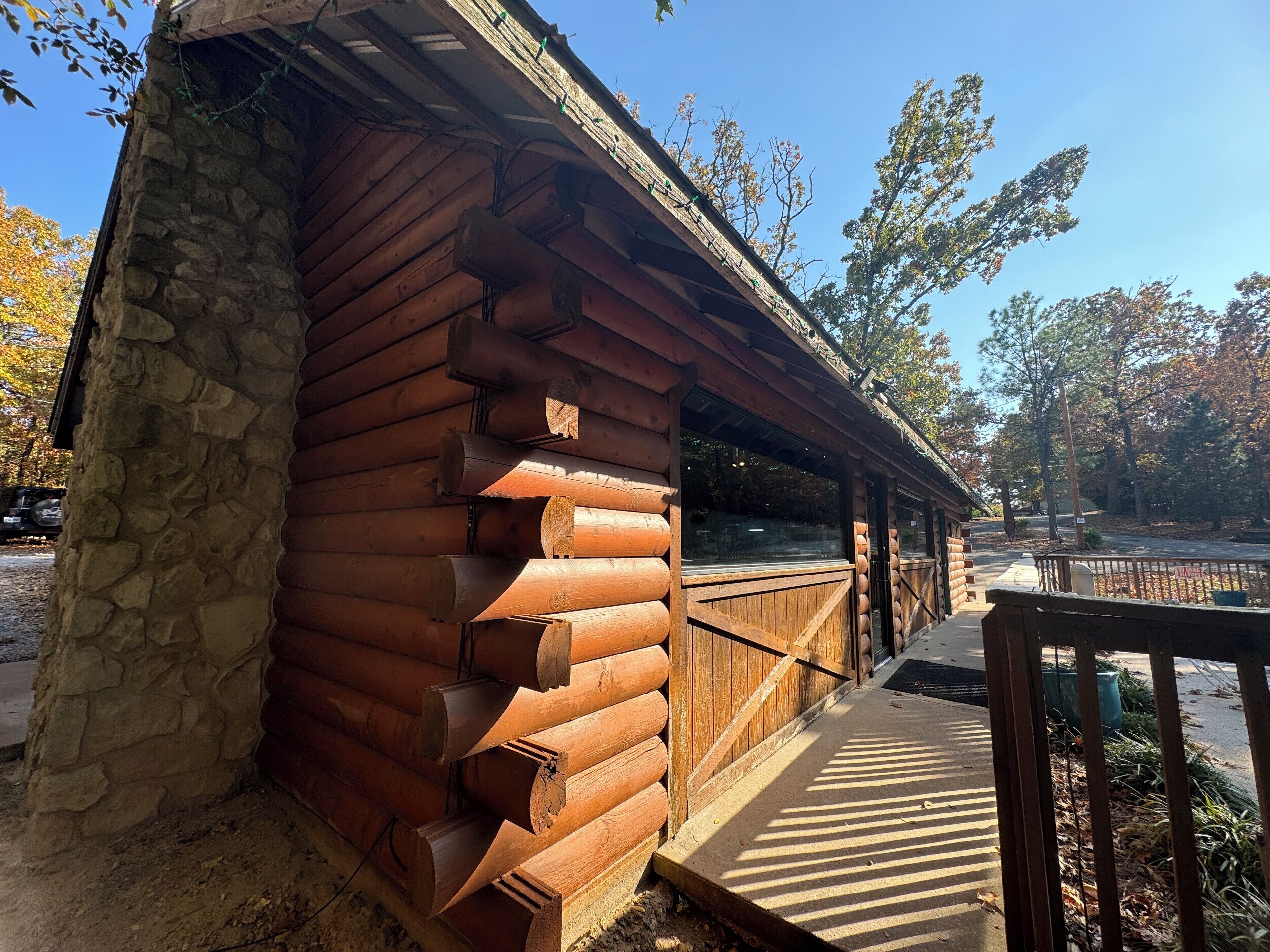 A wooden cabin with a stone foundation, a porch, and a view of the surrounding trees.