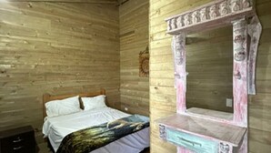 Una habitación de madera con una cama, un tocador con espejo y un reloj de pared.